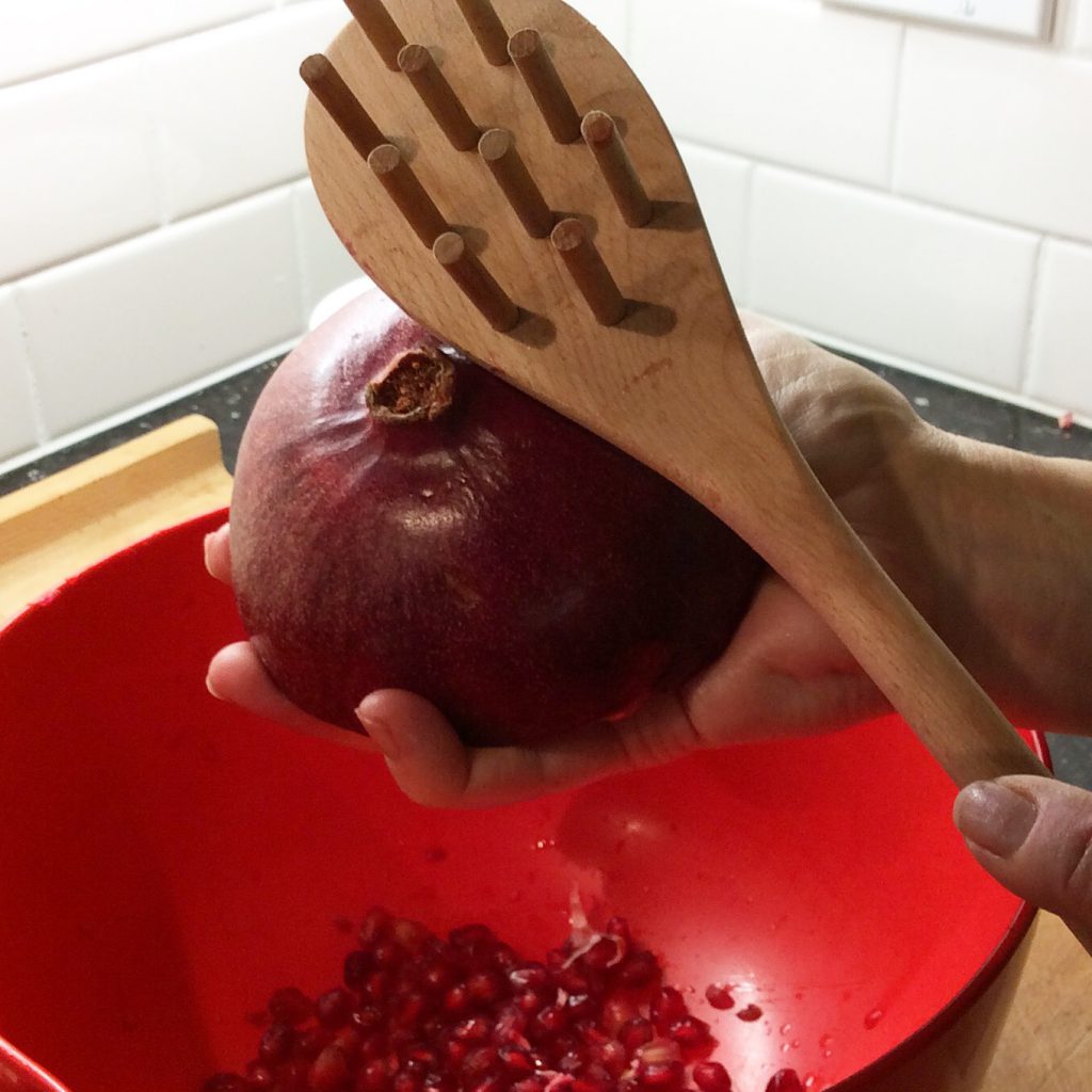 a wooden spoon is hitting a pomegranate